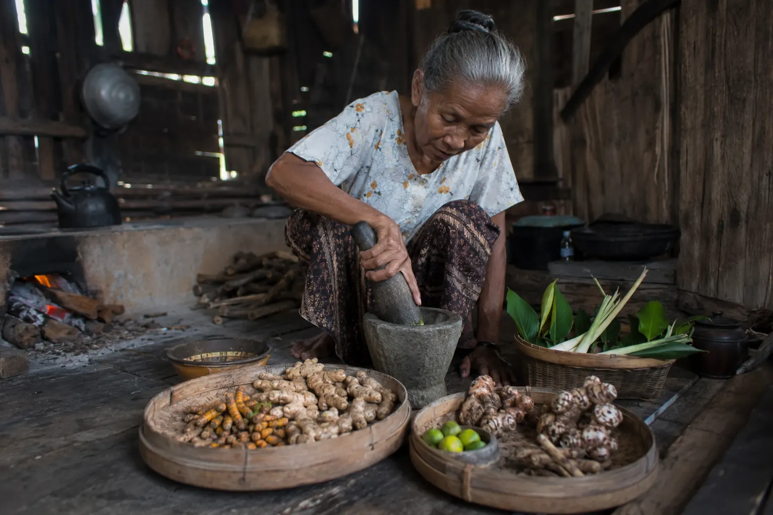 Femme javanaise préparant le jamu au mortier près du feu de bois
